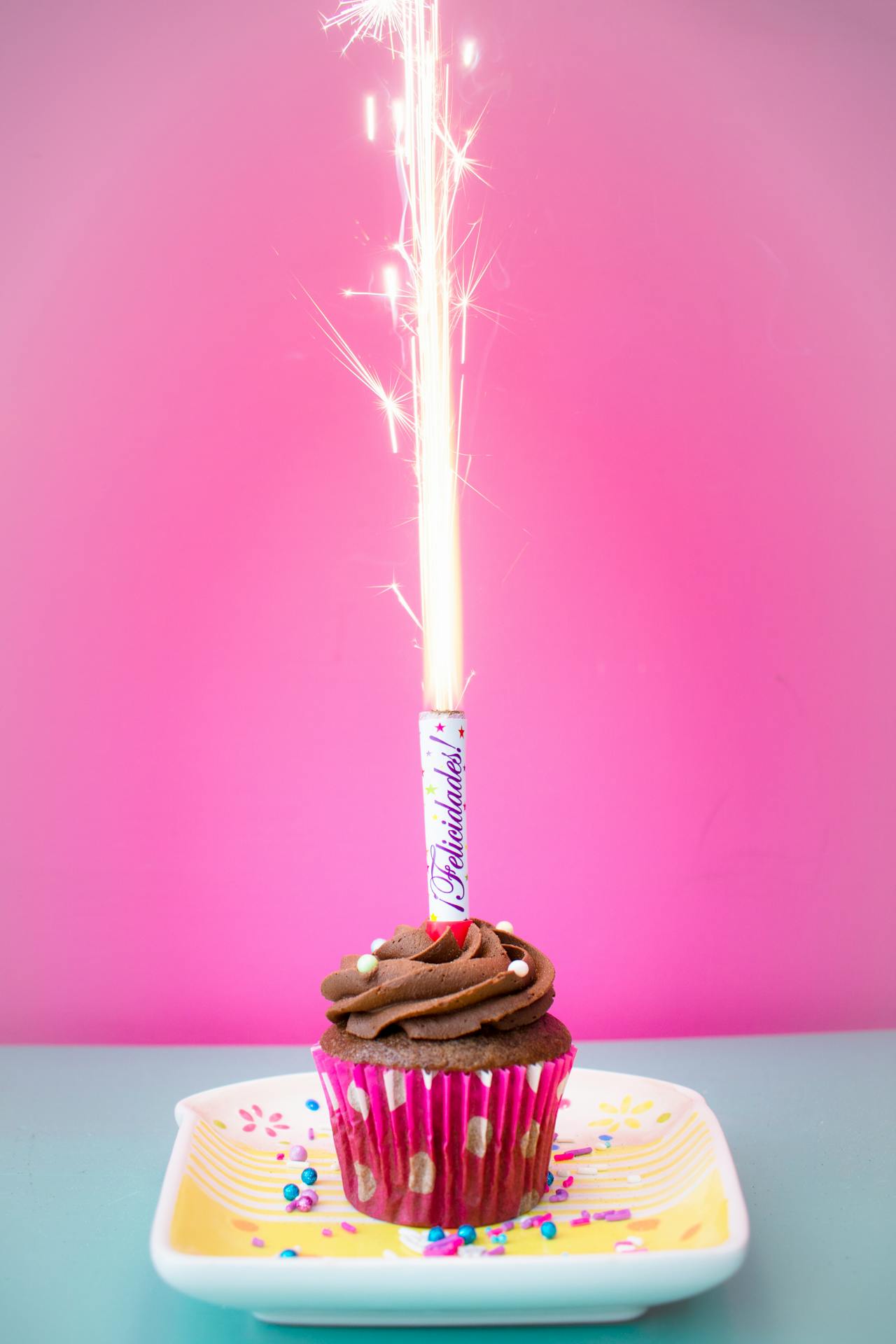 Cupcake on a plate with a sparkler on top.